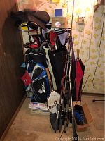 Overview of two golf bags filled with clubs, fishing poles, boxing gloves, and a tennis racket in a corner.