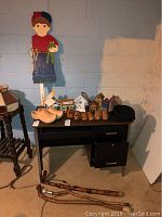 Wooden garden boy figure holding frog, wooden and ceramic birdhouses, wooden clogs on table, three canes on floor, two hats on table