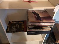 Shelf holding a stack of vinyl records including a visible album titled 'Olivia' by Olivia Newton-John and a separate album of Porgy and Bess soundtrack.