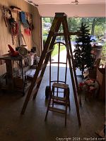 Wide view of the 6-foot wooden step ladder, 3-foot wooden step ladder, and red metal hand truck arranged inside a garage.