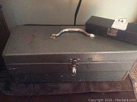 Closed metal toolbox with handle and latch, surface scuffed and lightly oxidized