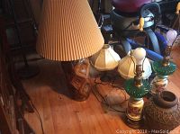 Wide view showing ceramic carved lamp with large beige pleated shade, two small fabric-shaded lamps, and two glass floral and green base lamps