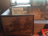 Framed forest landscape in wood frame with additional framed art behind on couch