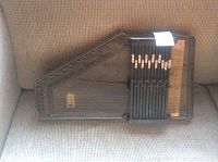 Full view of the vintage wooden harpsichord resting on a fabric surface showing the strings, keys, and wood body.
