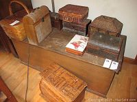 Eight wooden boxes and baskets arranged on and around a wooden trunk. Includes various sizes and shapes, some woven, some solid wood.