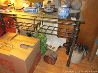 Photo showing the entire metal and glass table with two wire metal baskets underneath and some items placed on top and around the table.