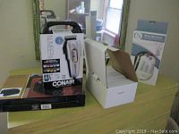 Image showing Conair haircutting kit box with multiple guard sizes indicated and tools visible, arm rest organizer, white product box for Distress Alert System LLR-100, and a boxed mini air compressor Elite-55E.