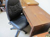 Wooden desk with three drawers alongside black rolling office chair