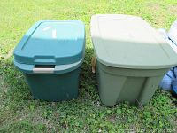 Two large plastic storage tubs with lids, one green and one gray, shown outdoors on grass