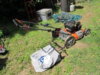 Side and top views of orange Husqvarna push lawn mower with black engine and attached leaf collection bag on grass backyard