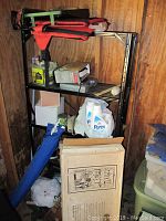 Metal shelving unit with cleaning supplies including detergents, a device charger, and various small hardware items and boxes.