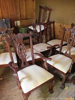 Eight vintage wooden dining chairs arranged in a room with two captain's chairs and six side chairs, carved wood with upholstered seats
