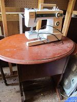 Janome sewing machine on reddish-brown wooden sewing table, showing full view of the machine and table shape.
