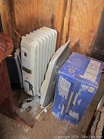 Oil heater, window fan, and boxed ceiling fan light kit together in a wooden storage area.