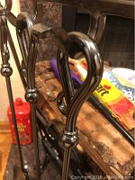 Close-up photo of wrought iron handles of fireplace tools showing decorative curved design.