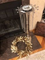 Tall metal floor candle holder with hanging beads and silver ball decoration, standing near fireplace, gold decorative wreath beside it