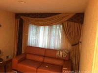 Full view of the window setup showing one set of gold curtains with brown valence above, sheer white curtain underneath, and couch below the window.