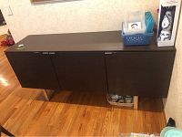 Front view of modern dark wood server with three closed doors and metal legs.
