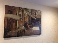 Full view of the stretched canvas print of an outdoor cafe scene hanging on a wall.