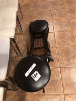 Top view of a black vinyl cushioned folding stool placed upside down showing the stool's seat size and black metal frame.