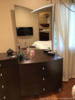 Front view of dark brown curved 3-drawer dresser with attached mirror and items on top