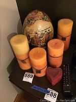 Overview of the lot showing five candles of various sizes with one large decorative Royal Satsuma egg on a wooden stand in the background.