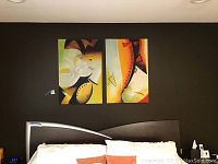 Two adjacent abstract oil paintings hung on a dark wall above a bed's headboard