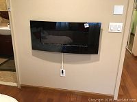 Front side view of Twin Star electric wall fireplace mounted on wall with visible black glossy finish and decorative stones inside glass panel.