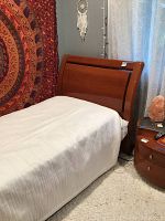 Full side view of the twin bed frame with white linens and wooden headboard adjacent to a colorful tapestry.