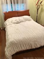 Front view of full sized wooden headboard with white comforter on bed frame.