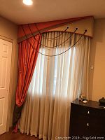 Wide view showing one silk window treatment panel with sheer inner curtain, rust-orange and olive green layered silk fabric, metal grommets, and decorative cords