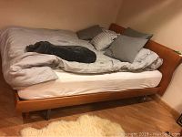 Photo showing side and footboard of queen wooden bed frame with bedding on top.