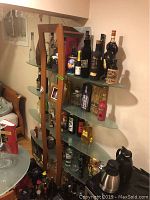 Full view of the wood and glass wall unit with surfboard-shaped glass shelves, showing various bottles and glassware on the shelves for scale and context.
