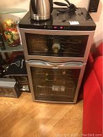 View of the Avanti two door wine cooler showing two doors with glass windows, wine bottles on metal racks inside, and digital control panel on top front.