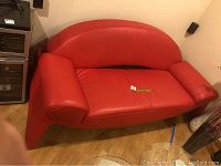 Full view of the modern red leather loveseat couch showing its curved backrest, armrests, and seat.