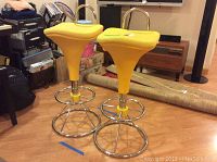 Two yellow swivel bar stools featuring plastic seats with fabric cover showing some wear and soiling, chrome circular bases, and adjustable height mechanism.