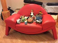 Front angle view of the red leather armchair showing the rounded arched back, wide armrests and chrome legs. Small scuff marks near the front right corner foot.