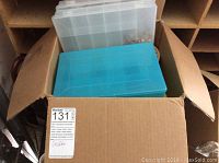 Closed cardboard box containing four plastic storage boxes and assorted ribbons inside