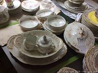 Full view of the china set with platter, covered vegetable bowl, cream soup bowls, plates, creamer and sugar bowl on a table.