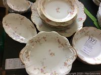 Various pieces from the Haviland china set including platters and multiple salad plates with pink floral decoration and gold trim.