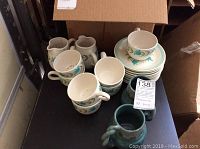 22-piece set on dark surface including Franciscan china cups, dessert plate, saucers, pitchers, and two green pottery cups