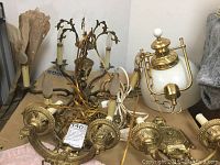Chandelier and two wall sconces piled on table showing candle-style bulb holders and white glass central fixture on chandelier.