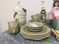 Photo showing full set of olive color stoneware dishes including stacked dinner plates, dessert plates, cups and saucers, salad bowls and soup bowls.