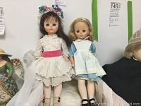 Front view of two Madame Alexander dolls sitting side by side, Degas Girl doll on left, Alice doll on right