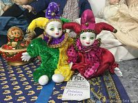 Two hand-painted porcelain clown figurines in colorful jester costumes seated on fabric.