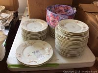 Stack of multiple Theodore Haviland plates in two floral patterns on a table with a floral fabric storage basket beside them.