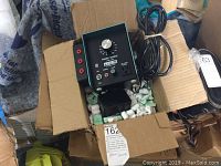 Power source unit in open cardboard box with packing peanuts, showing front and side panel with controls and power cord.