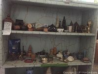Wide view of multiple wooden, ceramic, and metal trinkets arranged on two shelves of a distressed white wooden shelving unit.