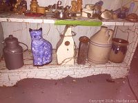 Photo showing six items arranged on a cracked white wooden shelf, including pottery, a birdhouse, and metal canister.