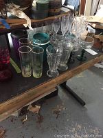 Various glassware pieces including tall champagne flutes, tall decorative tumblers with gold rim, clear ice cream sundae glasses with fluted design, and green stem glasses arranged on table.